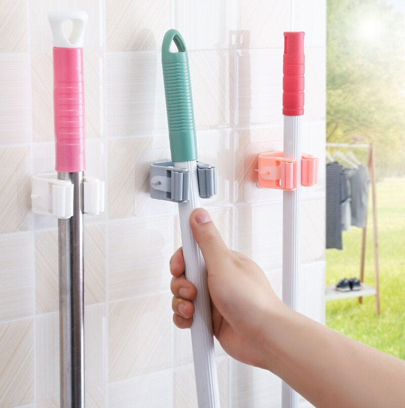 Mop and broom holders on a tiled wall with close-up of hand using holder.