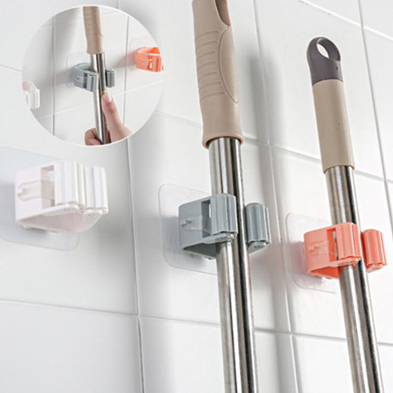 Mop and broom holders on a tiled wall with close-up of hand using holder.