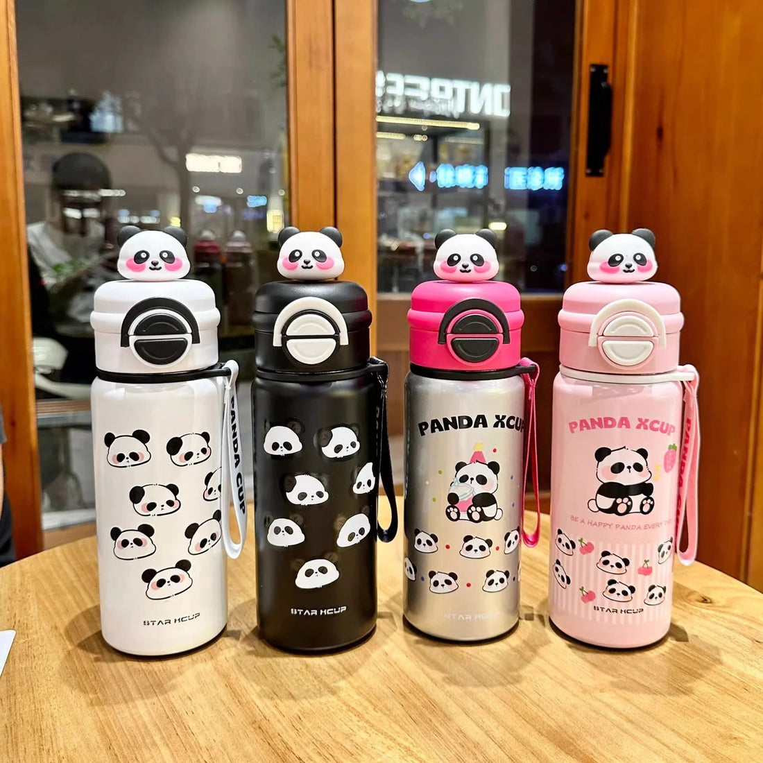 Pink panda-themed water bottle with a matching panda-shaped lid on a green surface.