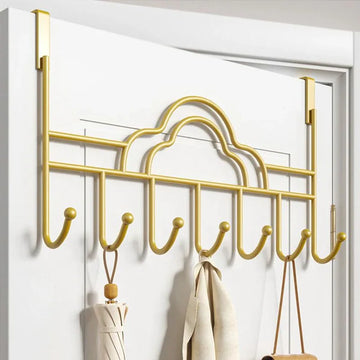 Gold over-the-door hook rack with clothes on a white door