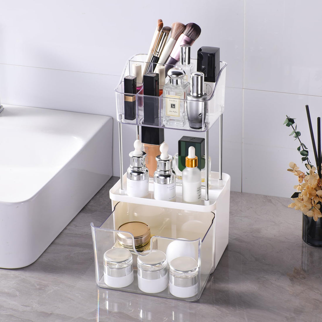 Clear acrylic cosmetic organizer with various items on a bathroom counter.