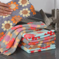 Stack of colorful patterned towels on a kitchen counter with a hand holding a towel.