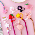 Various colorful straw tips with cartoon designs on a pink background