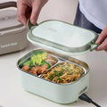Heated lunch box with compartments filled with food, being held open by a person.