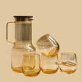Set of amber glassware including a carafe and three glasses on a beige background