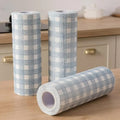 Three rolls of plaid-patterned tape on a wooden surface with a kitchen background.