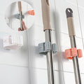 Mop and broom holders on a tiled wall with close-up of hand using holder.
