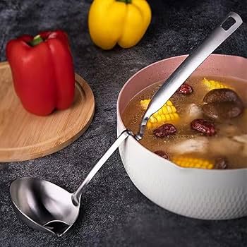 Bowl of soup with a spoon, red pepper, and yellow bell pepper on a dark surface