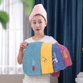 Woman holding colorful towels with a pink towel on her head indoors.