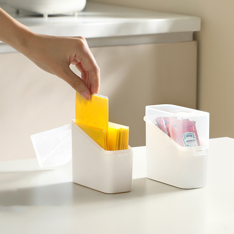 White container with compartments holding yellow and pink packets on a light surface.