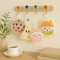 Four cute character-themed keychains hanging on a hook with a cup of coffee and books on a table.