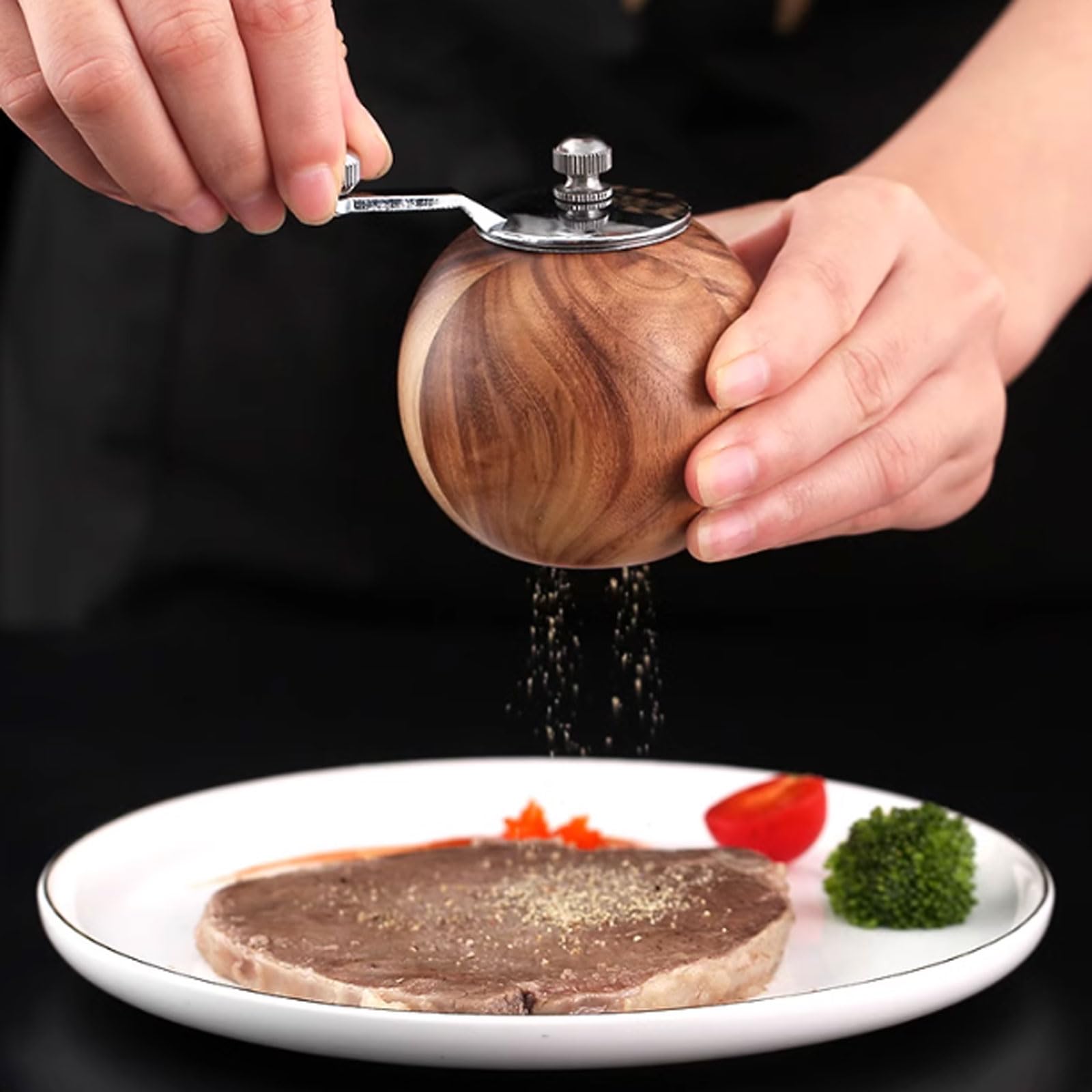 Person seasoning a dish with a wooden salt grinder on a black background