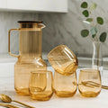 Set of amber glassware including a carafe and tumblers on a light surface.