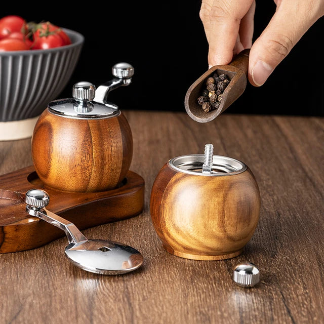 Wooden salt and pepper shakers with a hand adding black pepper, on a wooden surface.