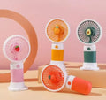 Four portable fans shaped like fruits on a pink and beige background