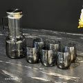 Set of smoked glass tumblers and a carafe on a marble surface with a dark background.