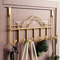 Gold over-the-door hook rack with keys, umbrella, and cap on a wooden door.