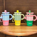Three colorful children's sippy cups with checkered sleeves on a wooden surface.