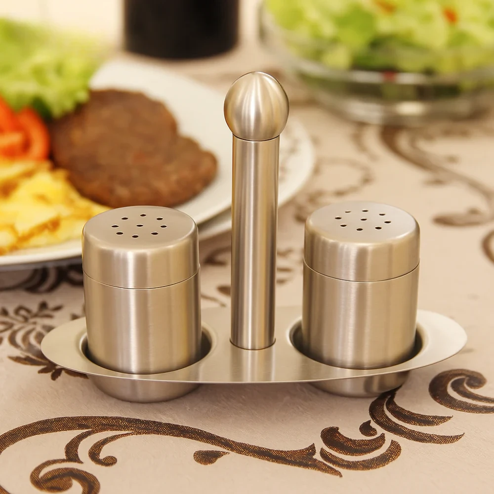 Stainless steel condiment set on a decorative tablecloth with food in the background